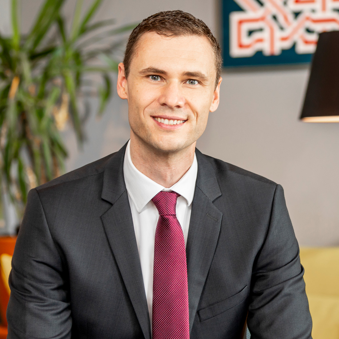 Dr. Bernd Kissling, Anwalt für Erbrecht in Heidelberg, sitzt in einem modernen Büro, trägt einen dunklen Anzug mit roter Krawatte und lächelt freundlich in die Kamera
