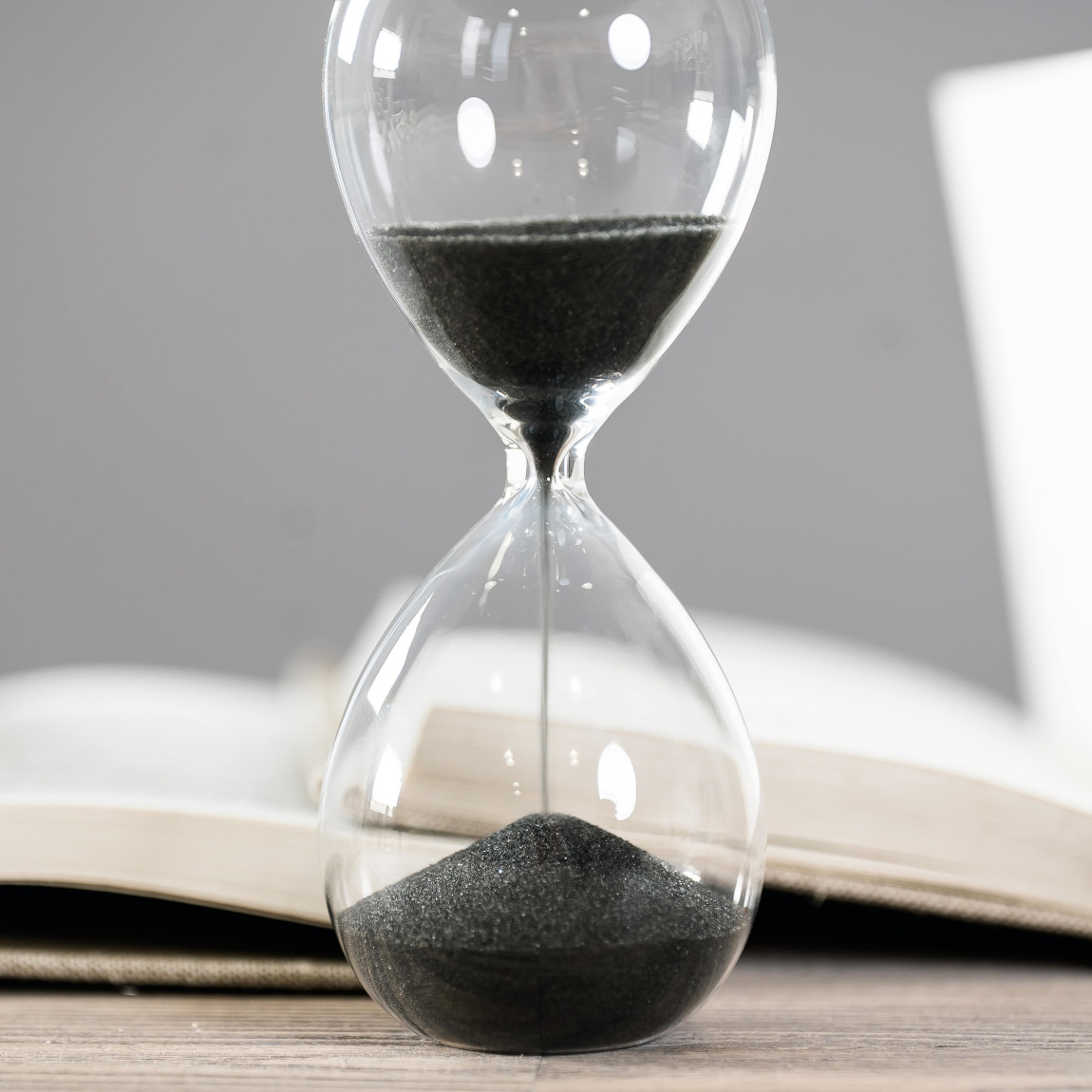 Eine Sanduhr mit schwarzem Sand steht vor einem geöffneten Buch, symbolisiert die begrenzte Zeit zur Vorbereitung vor dem Erbfall