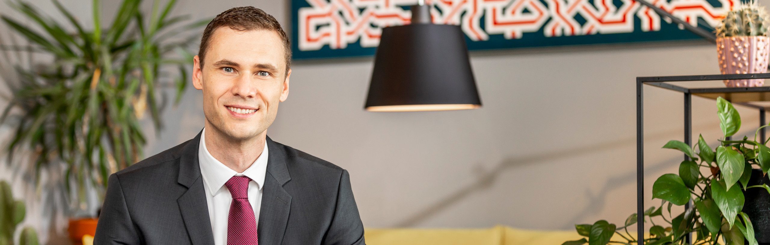 Dr. Bernd Kissling, Anwalt für Erbrecht, sitzt lächelnd in einem modernen Büro mit Pflanzen und Dekorationen im Hintergrund, trägt einen dunklen Anzug mit roter Krawatte