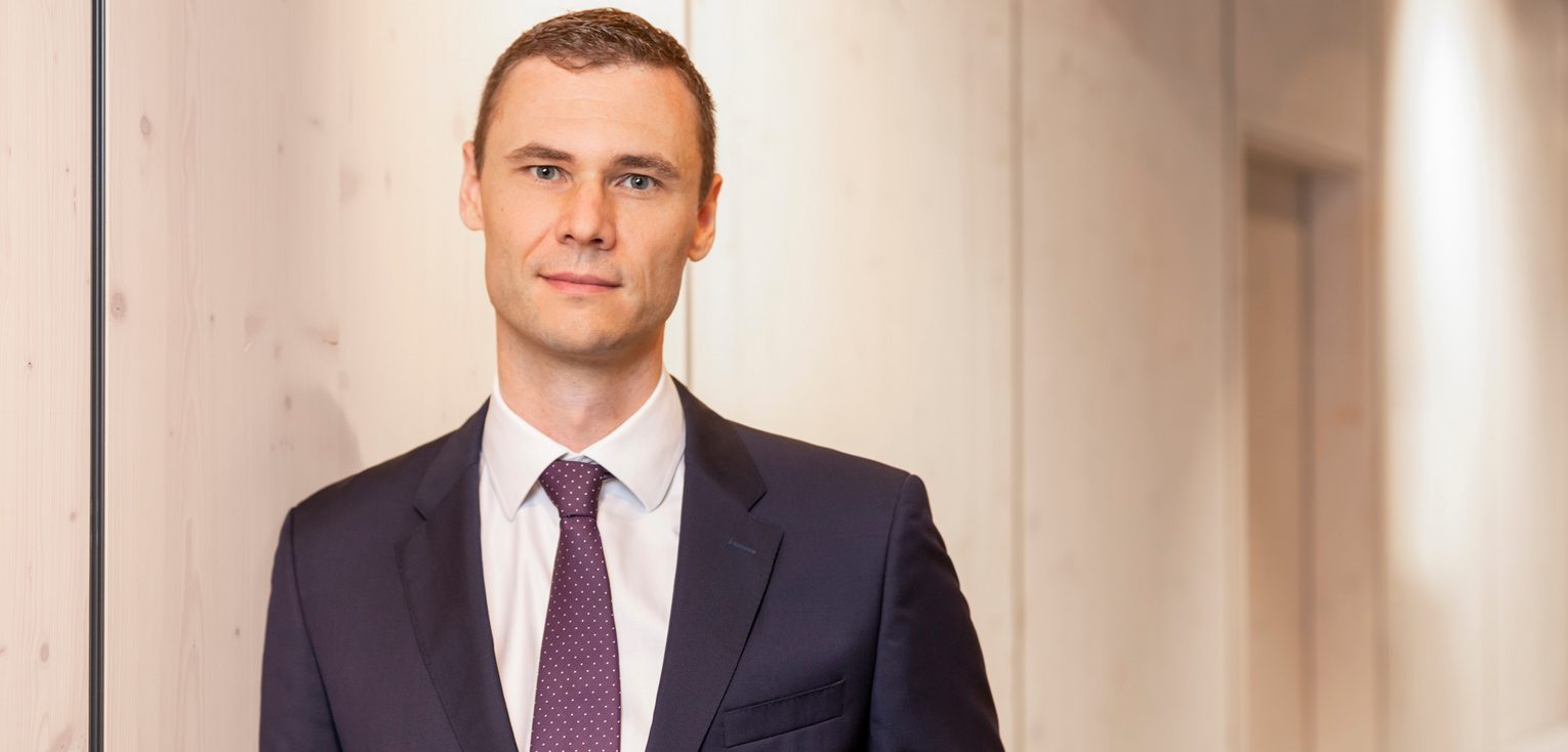 Dr. Bernd Kissling, Anwalt für Erbrecht in Heidelberg, steht in einem modernen Büroflur, trägt einen dunklen Anzug mit Krawatte und blickt in die Kamera